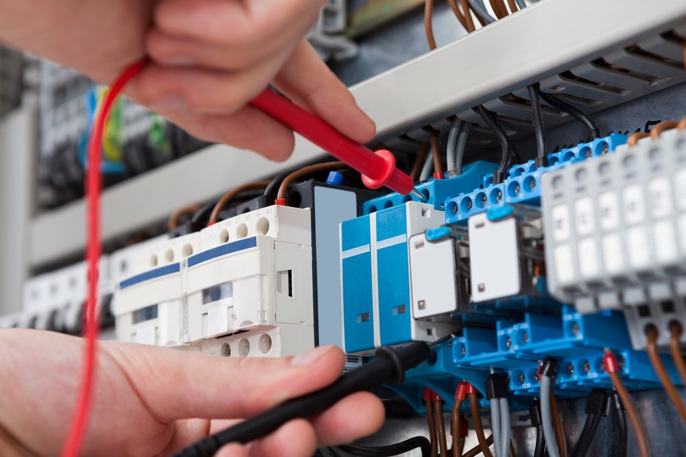 Closeup of male electrician examining fusebox with multimeter probe